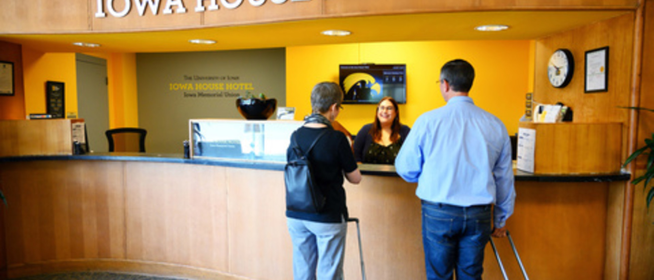 Image of the front desk of the Iowa House Hotel, displays two guests checking in as well as a receptionist